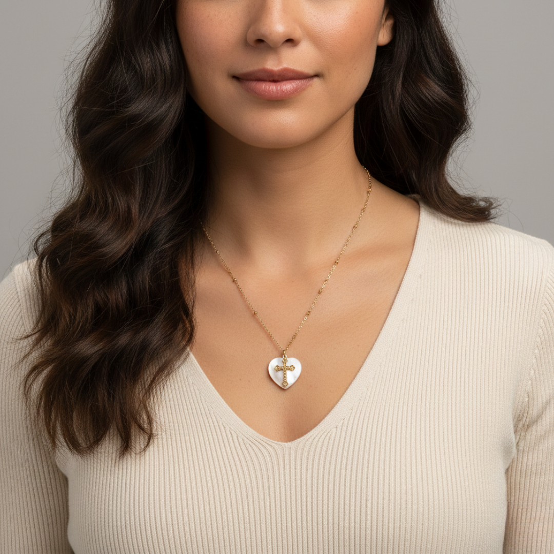 Woman wearing a gold necklace with a heart-shaped cross pendant against a neutral background