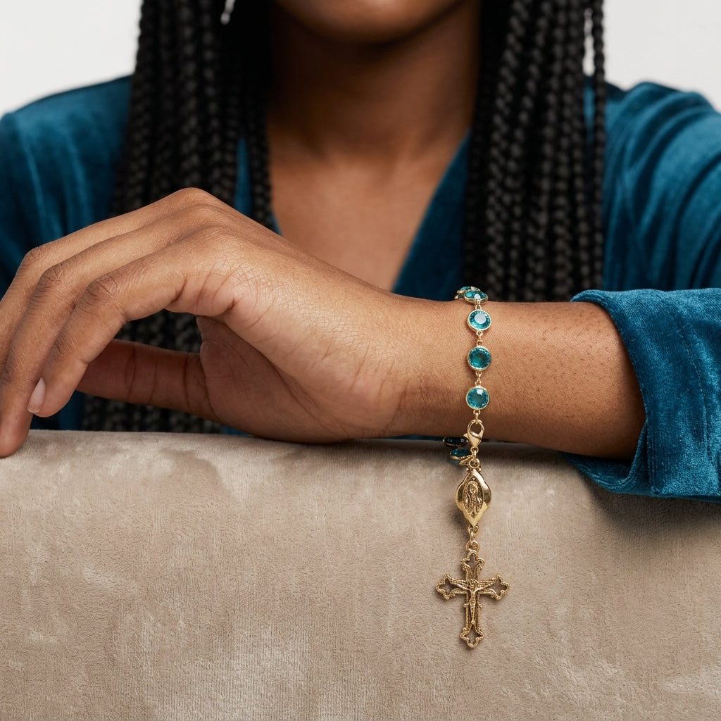 Person wearing a gold bracelet with blue crystals and a cross charm on a neutral background