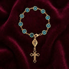 Gold rosary cross charm bracelet with blue crystals on a maroon fabric background