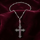 Silver tone cross pendant necklace with amethyst crystal accents resting on a burgundy colored fabric