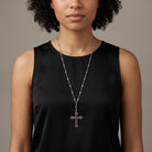 Woman wearing a silver tone necklace with a cross pendant and amethyst purple crystals 