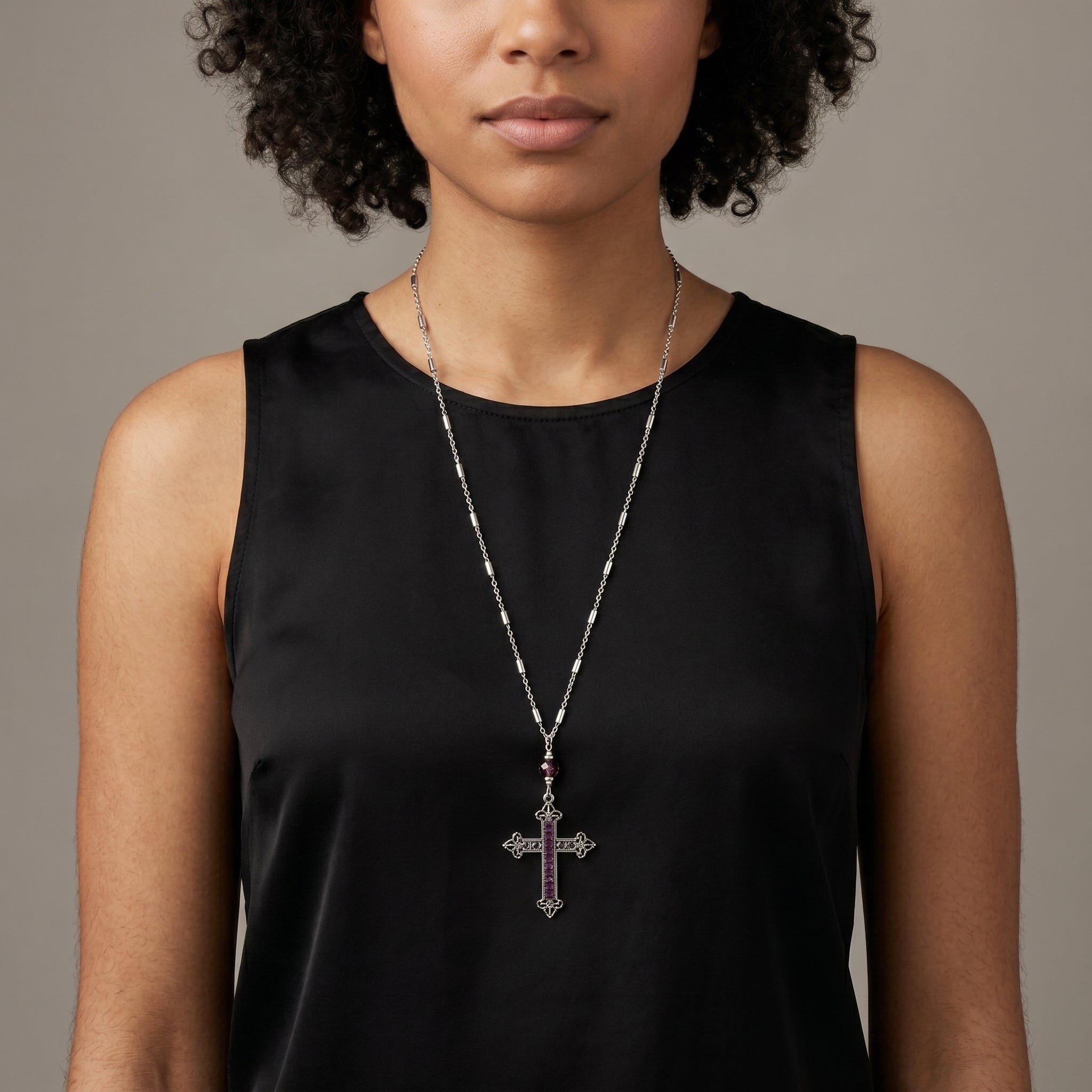 Woman wearing a silver tone necklace with a cross pendant and amethyst purple crystals 