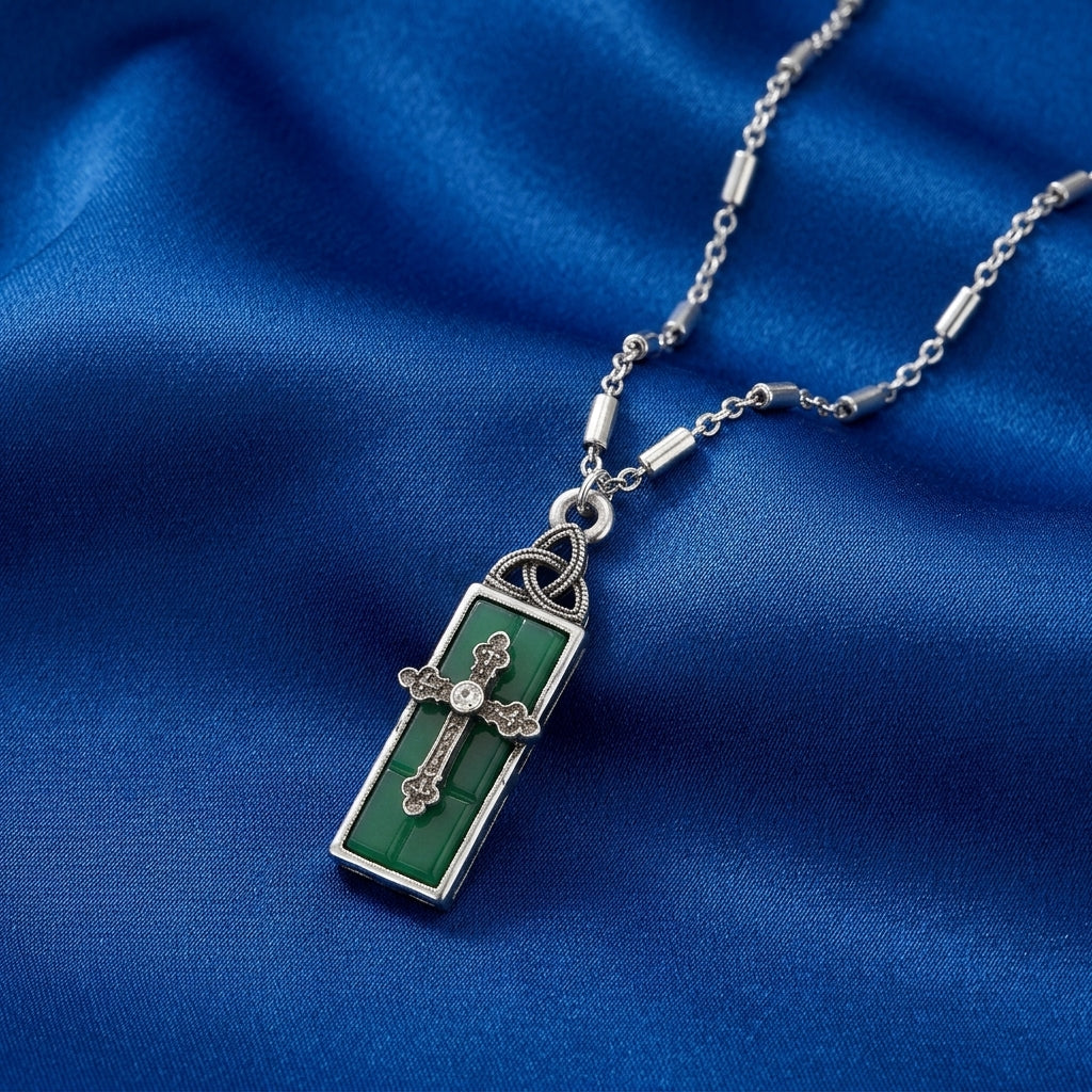 Green cross pendant with silver chain on a blue fabric background