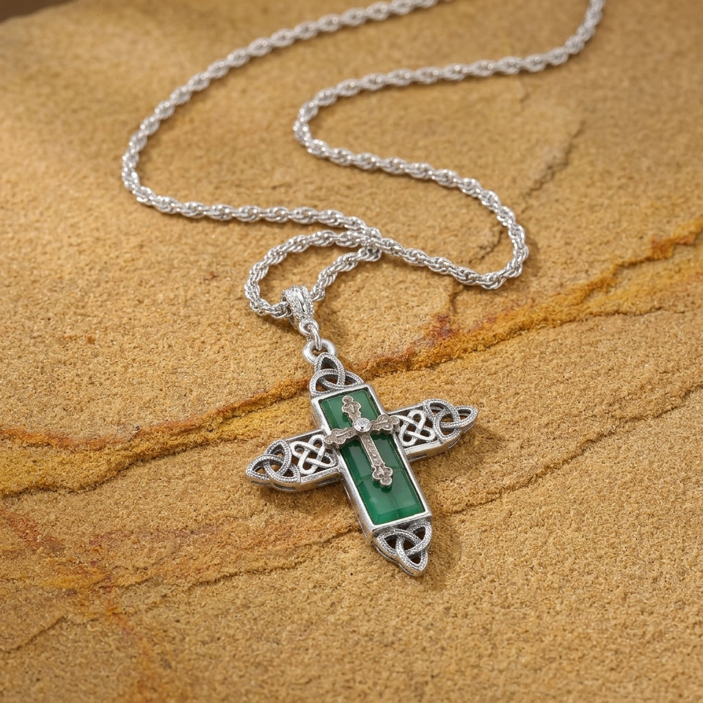 Silver cross pendant with green stone on a chain against a brown stone background