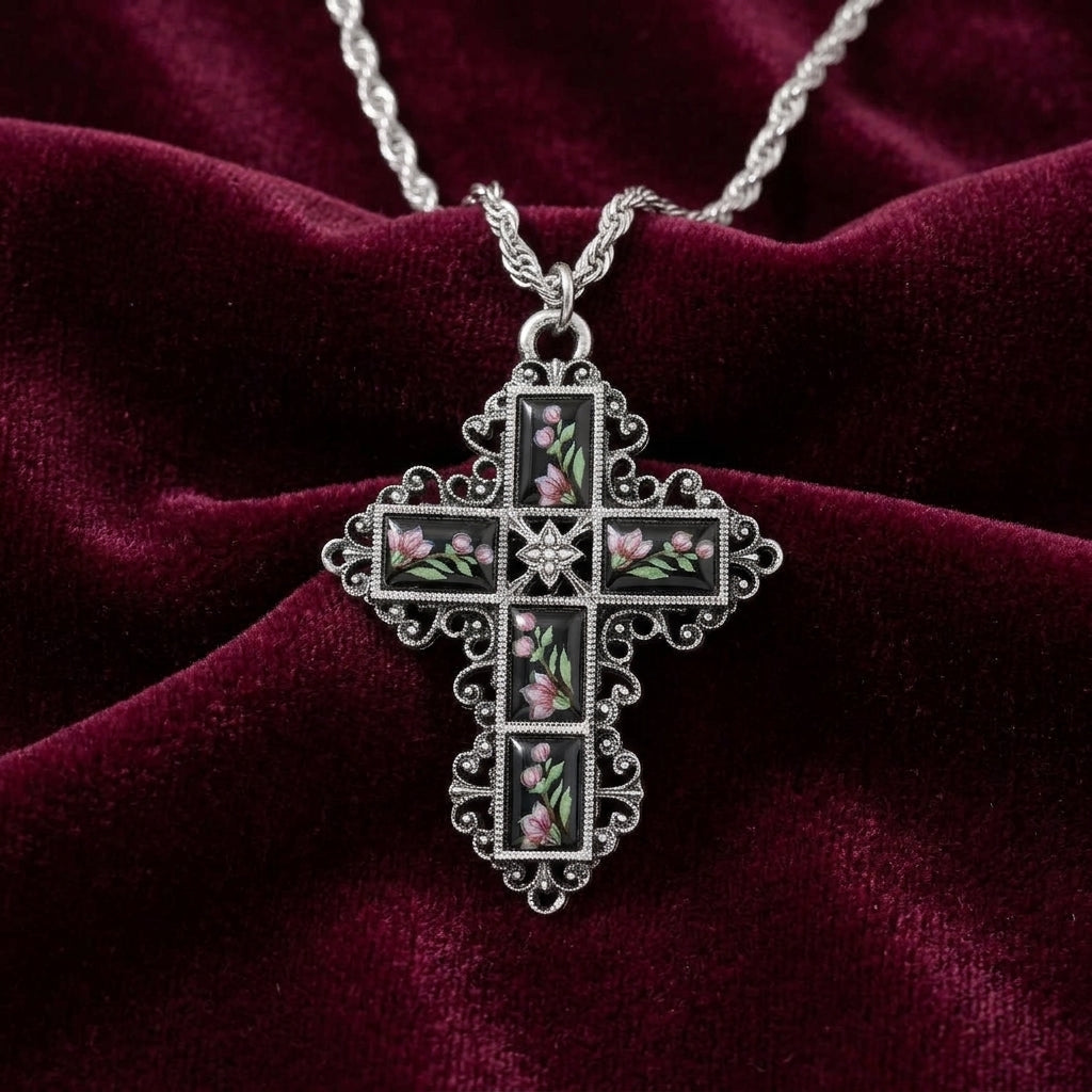 Silver cross pendant with black enamel stones and pink floral designs on a red velvet background