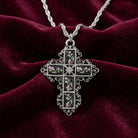 Silver cross pendant with black enamel stones and pink floral designs on a red velvet background