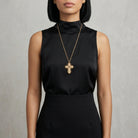 Woman wearing a black sleeveless top with a gold cross necklace against a gray background