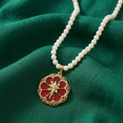 Pearl necklace with a red and gold cross and floral pendant on a green fabric background