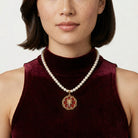 Woman wearing a faux pearl necklace with a red floral and cross pendant on a plain background