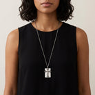 Woman wearing a black sleeveless top with a silver necklace featuring a cross pendant.