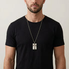 Man wearing a black t-shirt and a necklace with a cross pendant on a plain background