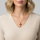 Woman wearing a gold necklace with a cross pendant on a plain background