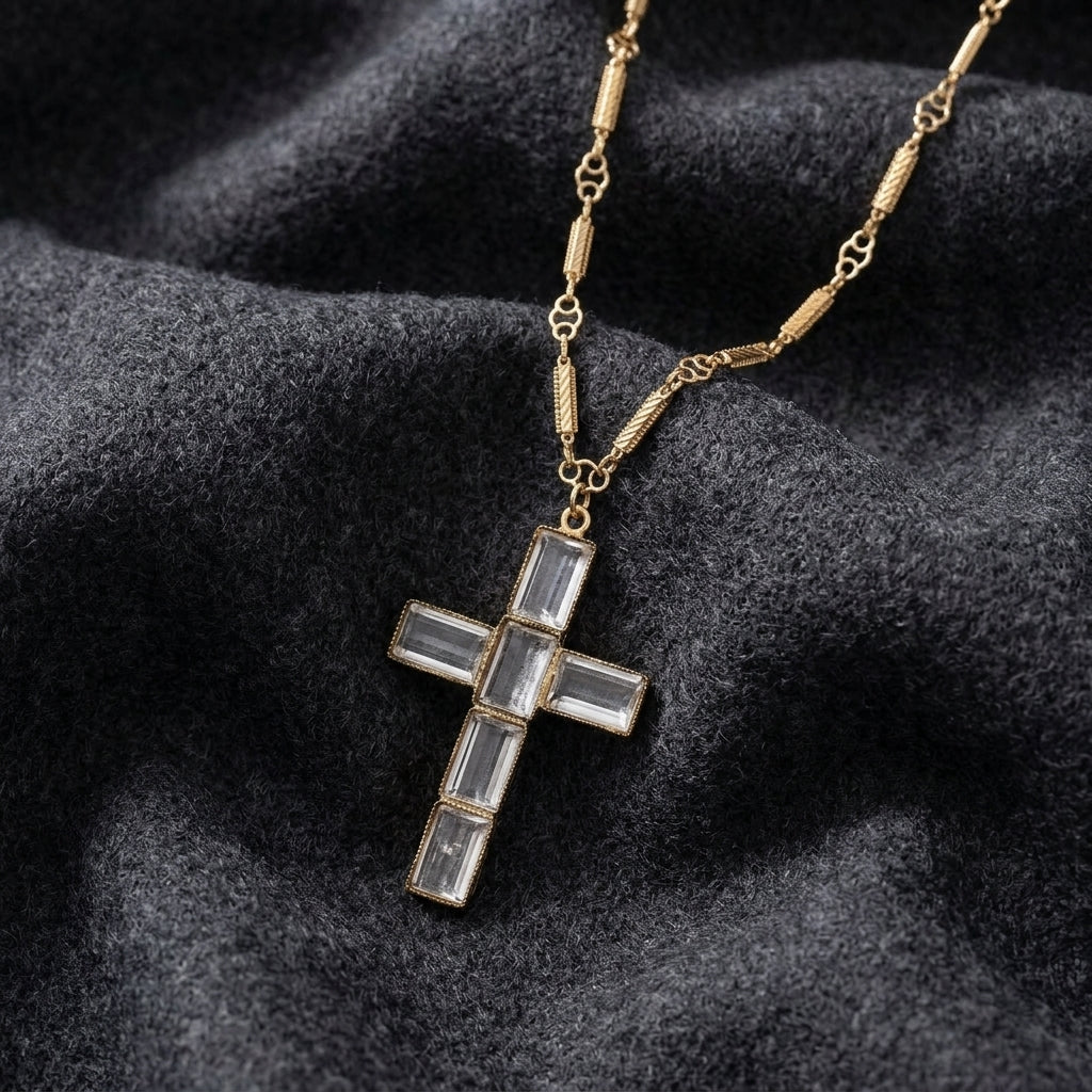 Gold cross necklace with embedded crystals on a textured dark surface