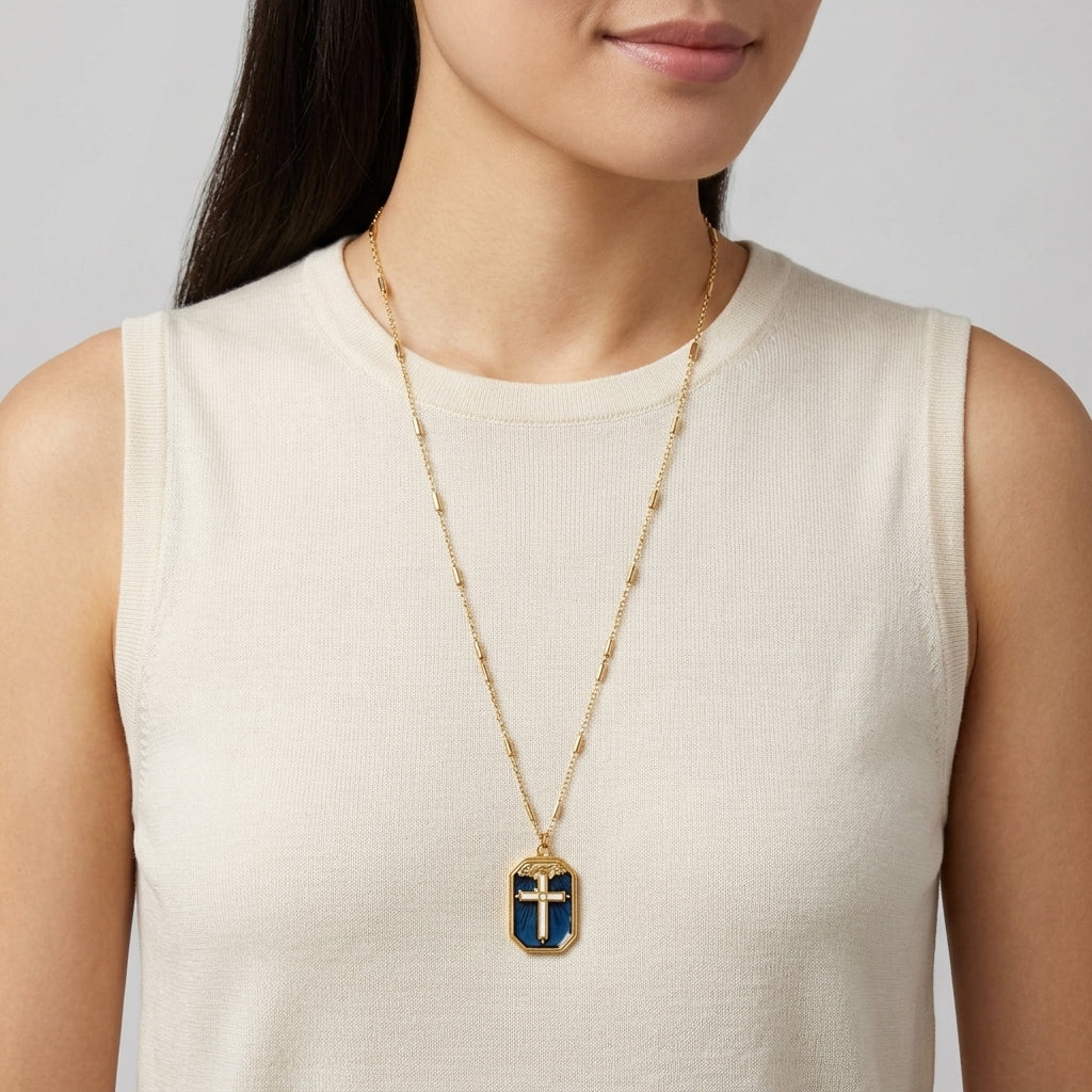 Woman wearing a gold necklace with a blue cross pendant on a plain background
