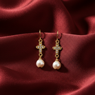 Gold cross earrings filled with clear crystals with faux pearl drops on a red fabric background