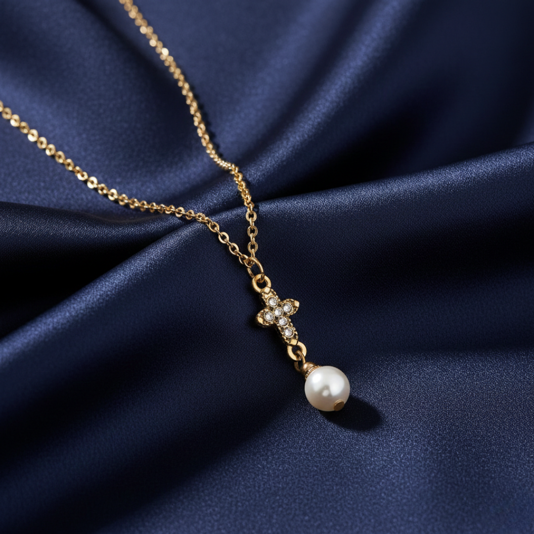 Gold necklace with a cross and faux pearl pendant on a blue fabric background