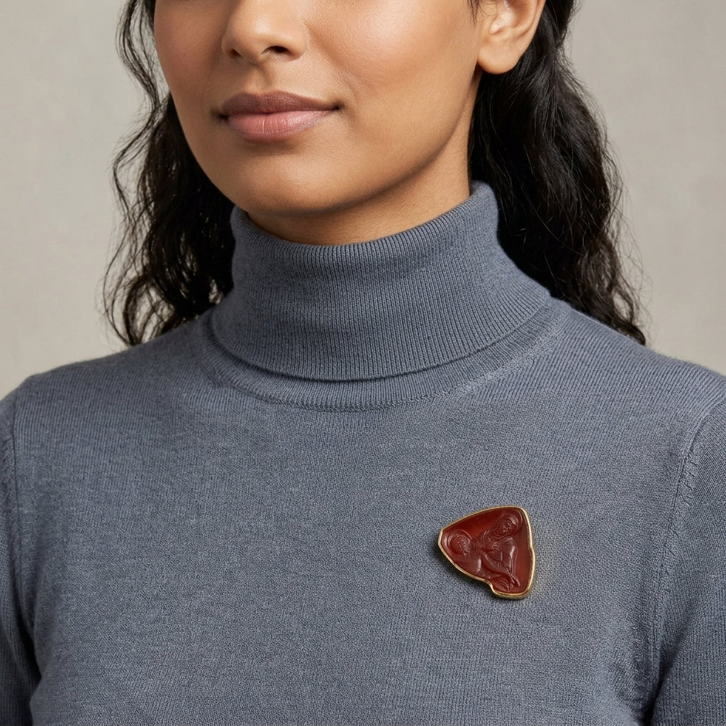 Person wearing a gray turtleneck sweater with a carnelian red Mother Mary and Jesus brooch on a neutral background