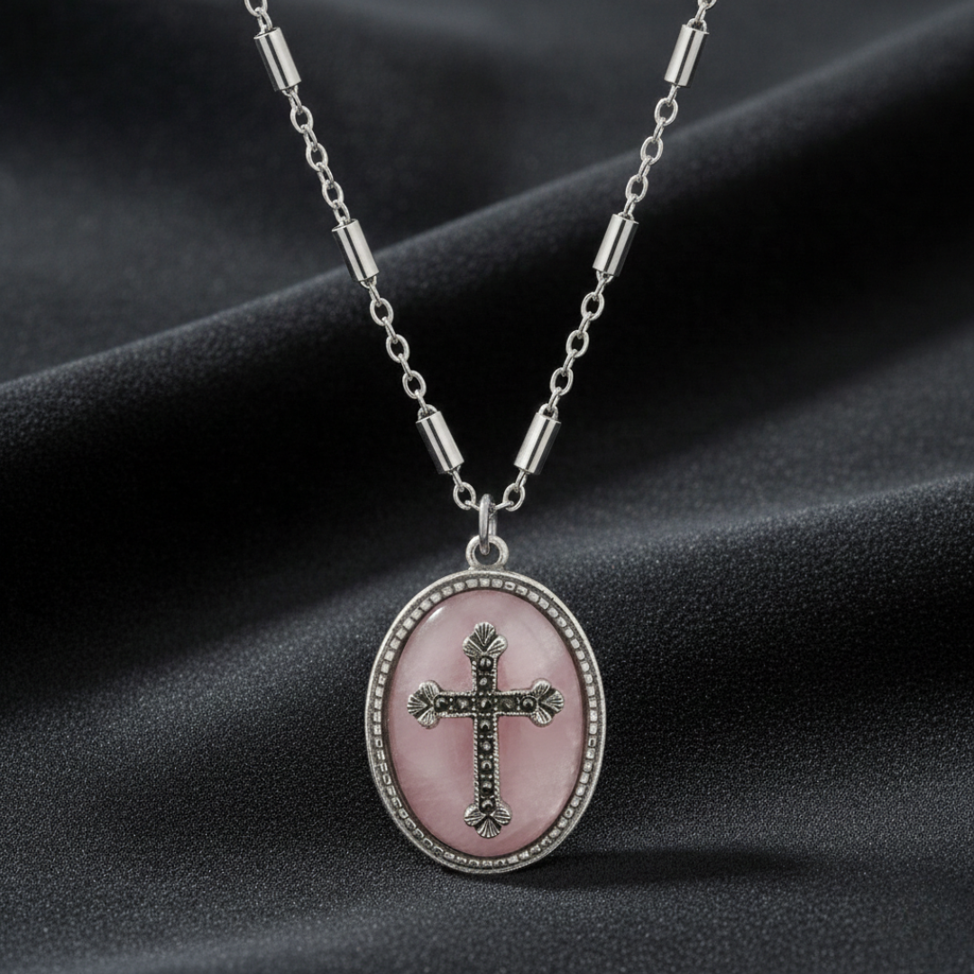 Necklace with a pink oval pendant featuring a cross on a dark fabric background