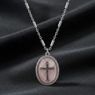 Necklace with a pink oval pendant featuring a cross on a dark fabric background