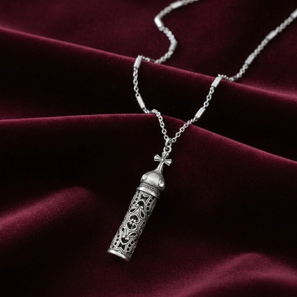 Silver necklace with a cross vial pendant on a maroon fabric background