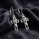 Silver cross earrings with feather designs on a dark fabric background