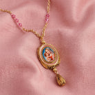 Gold necklace with a spinner pendant and pink glass beads featuring a religious scene on a pink fabric background