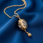 Religious motif gold tone spinner necklace resting on dark blue fabric surface. 