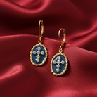 Gold earrings with blue enameled cross designs on a red satin background