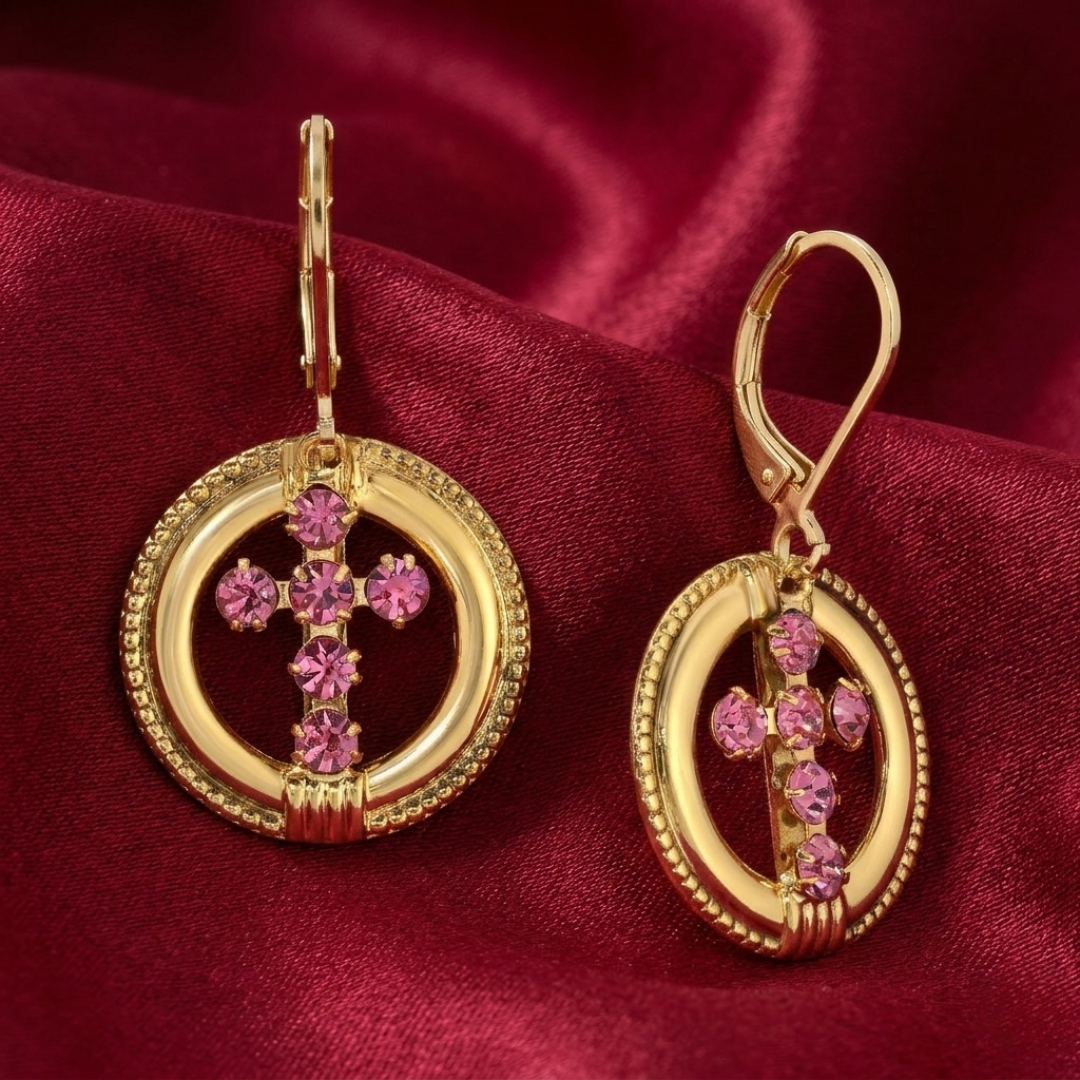 Gold cross earrings with pink crystals on a red fabric background