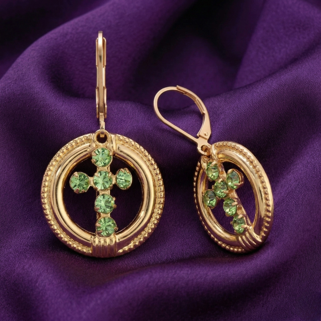 Gold cross earrings with green crystals on a purple fabric background