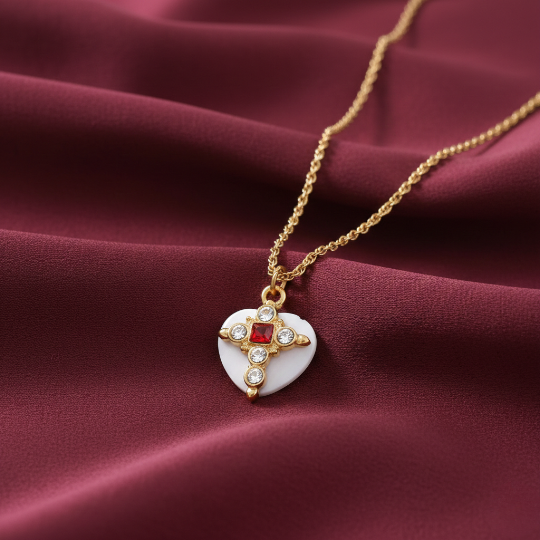 Necklace with a heart-shaped pendant featuring a red gemstone and gold accents on a maroon fabric background.