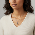 Woman wearing a necklace with a pearl cross pendant against a neutral background