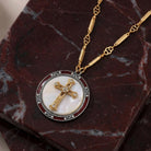 Gold tone cross pendant with clear crystal accents resting on a red marble surface