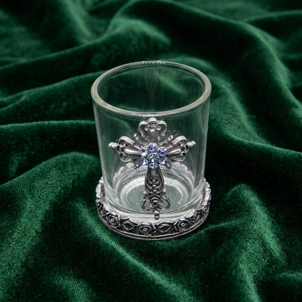 Clear glass candle holder with a silver cross and blue crystal accents on a green fabric background