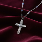 Silver cross necklace with floral design on a burgundy fabric background