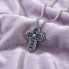 Pewter blue crystal cross pendant necklace with clear crystal accents resting on a purple fabric surface. 