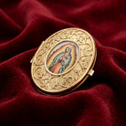 Gold tone pill box with Our Lady of Guadalupe motif on a red fabric background