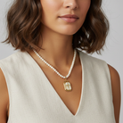 Woman wearing a pearl necklace with a gold pendant against a neutral background