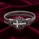 Silver bracelet with crystal accents and a decorative clasp on a burgundy fabric background