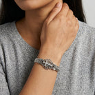 Close-up of a person wearing a silver cross bracelet with crystal accents on a neutral background