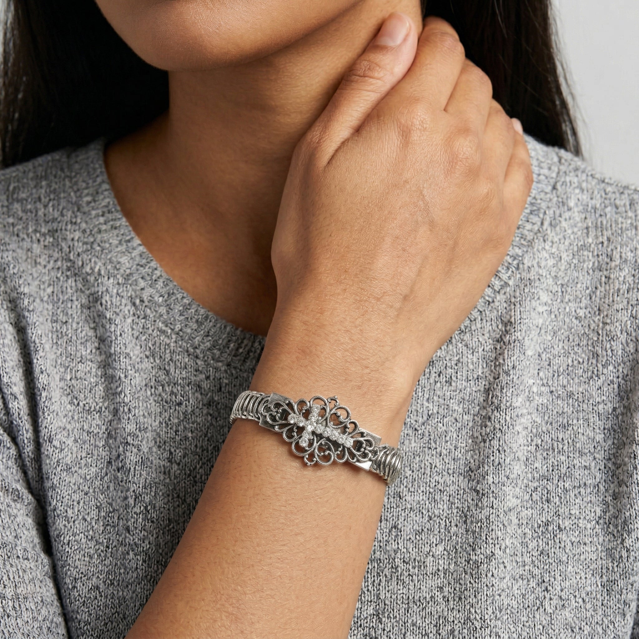 Close-up of a person wearing a silver cross bracelet with crystal accents on a neutral background