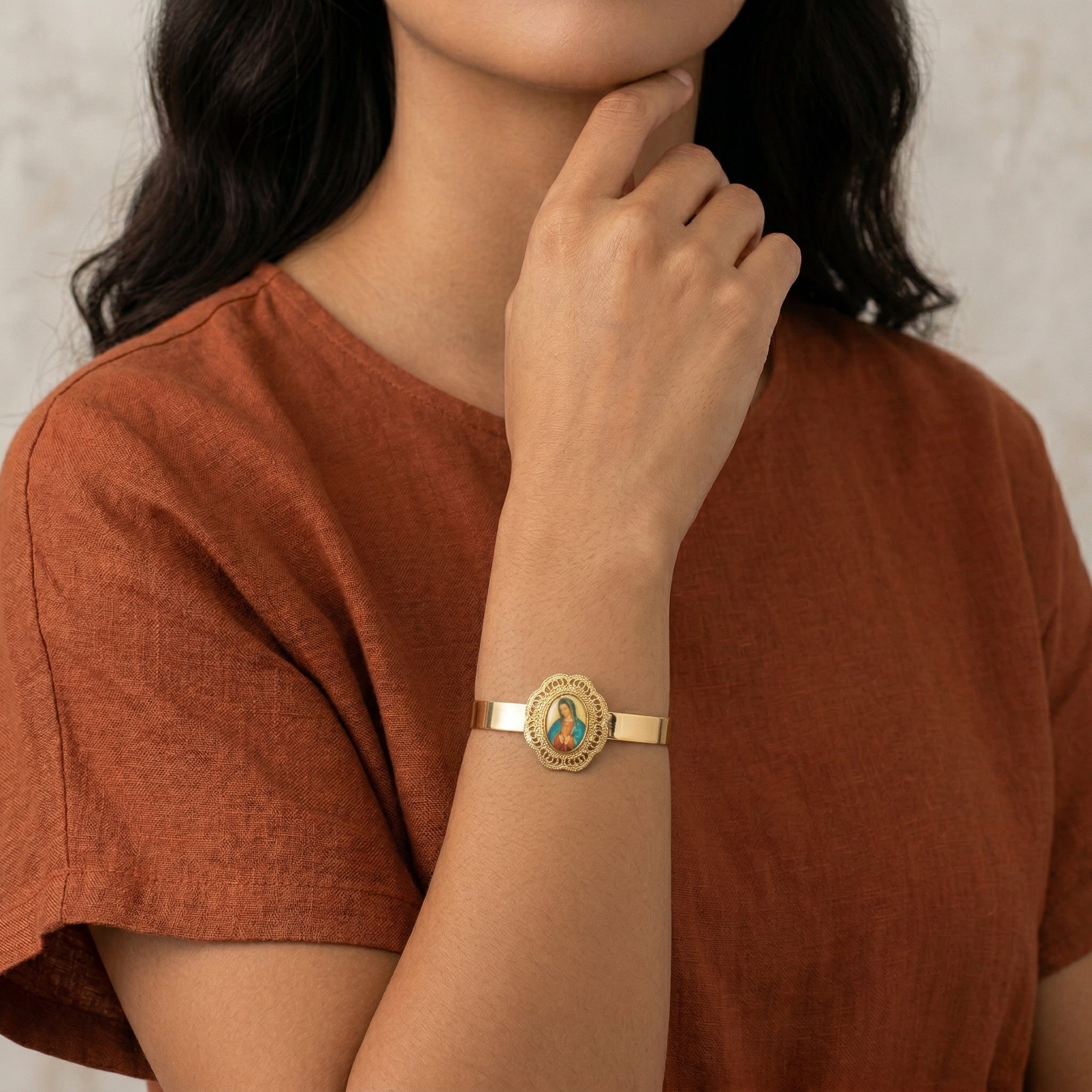 Woman wearing a gold bracelet with a circular religious design on her wrist, against a neutral background.
