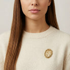 Close-up of a person wearing a cream sweater with a gold religious brooch.