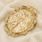 Gold religious brooch with intricate design on a beige fabric background