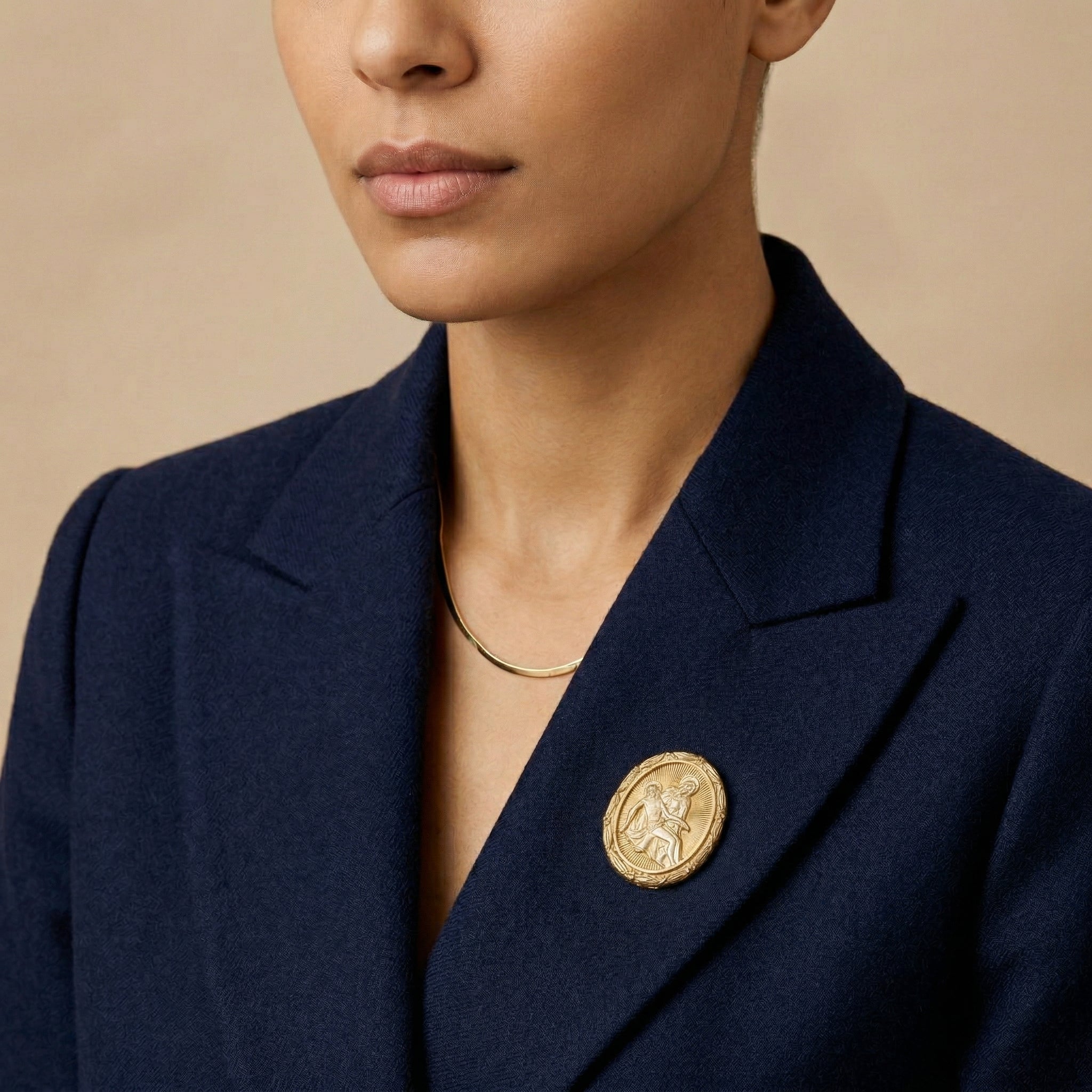 Navy blazer with a gold religious brooch worn by a person on a beige background