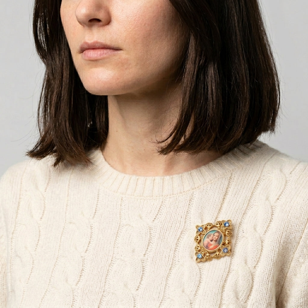 Woman with a cream-colored sweater wears a Mary and Child golden brooch with blue crystal accents