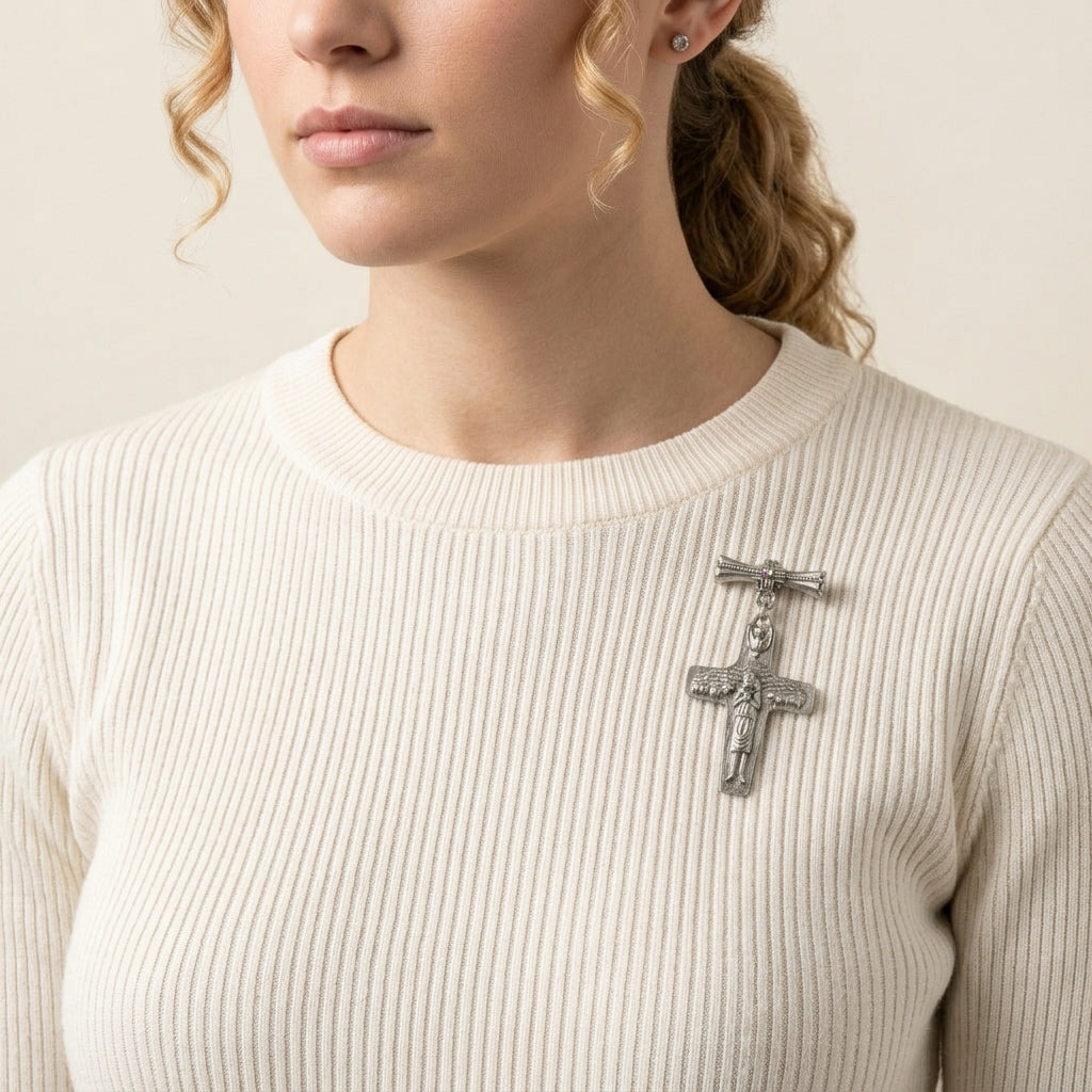 Woman wearing a silver cross brooch on a beige sweater against a neutral background