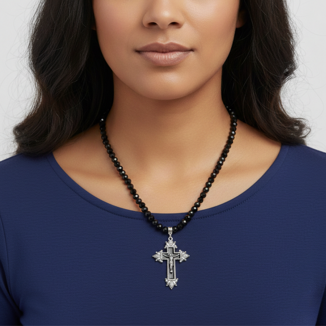 Woman wearing a black beaded necklace with a silver cross pendant on a plain background