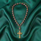 Necklace with pink beads and a gold cross pendant on a green fabric background