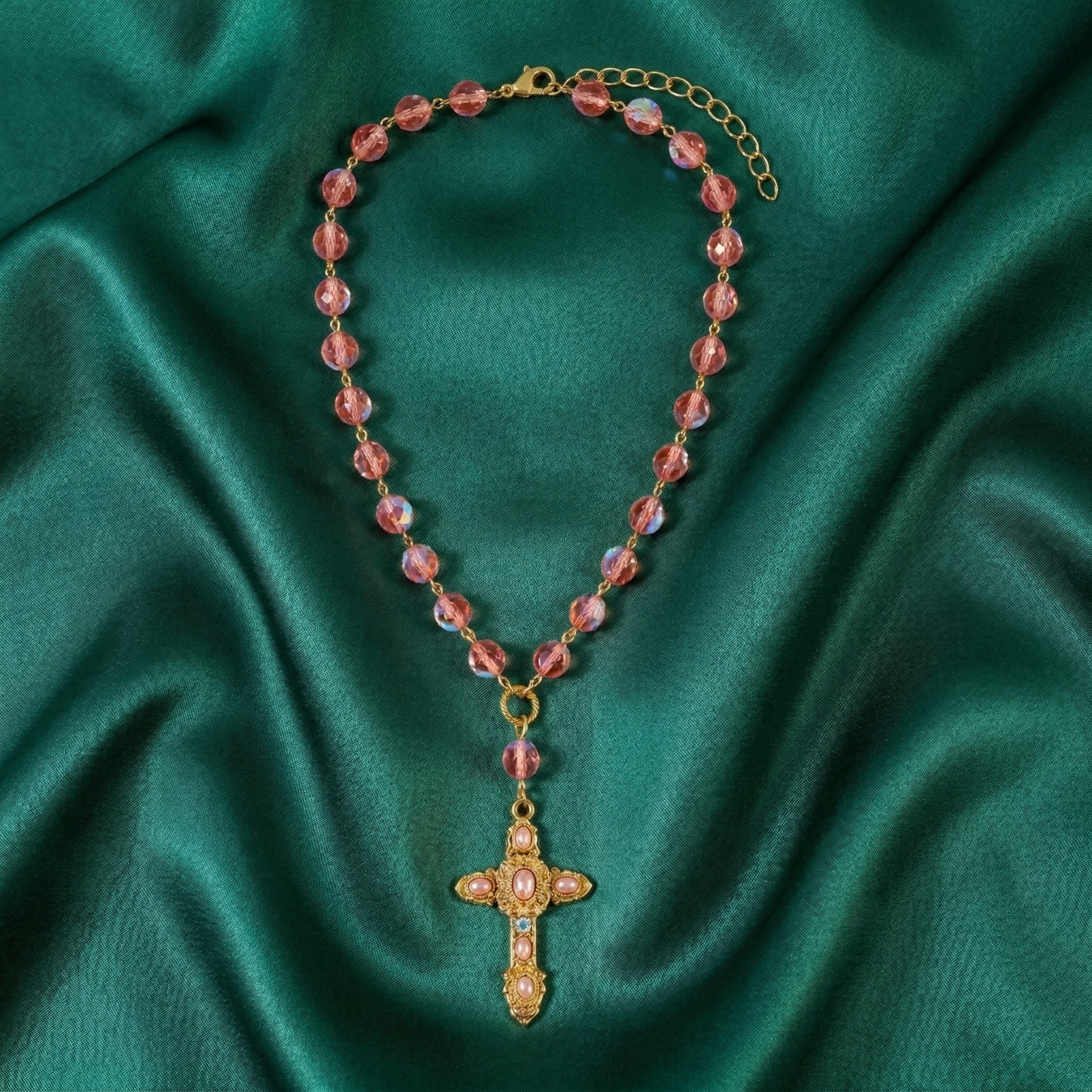 Necklace with pink beads and a gold cross pendant on a green fabric background